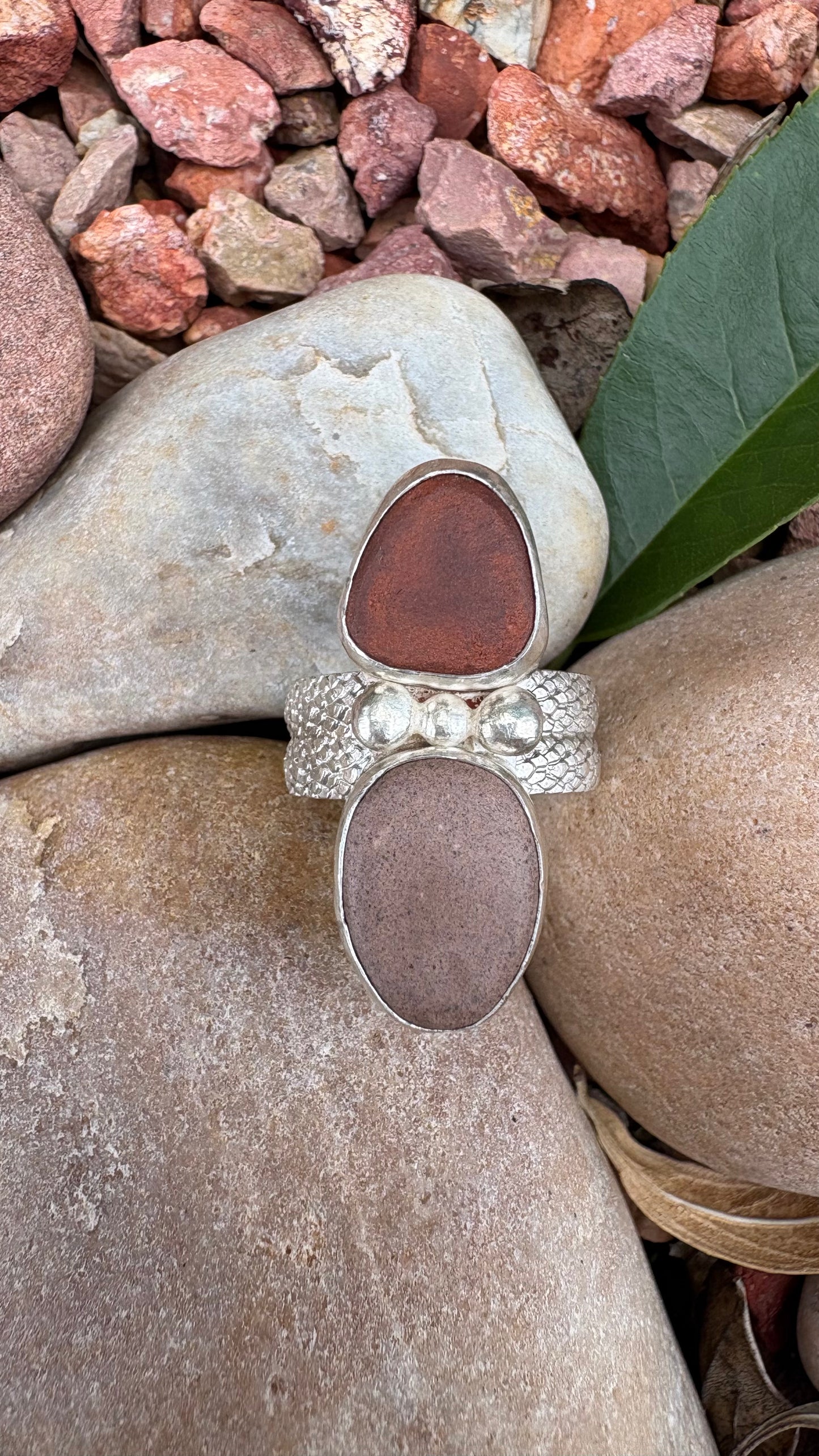 Silver ring with two large brown stones on a stone surface with pebbles and a leaf in the background.