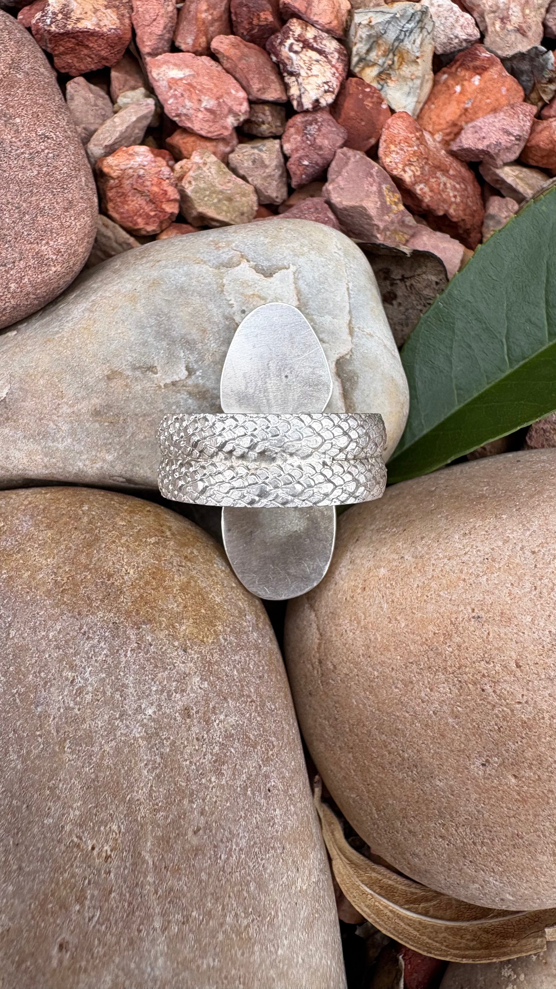 Silver ring with a clear stone on a bed of rocks and leaves