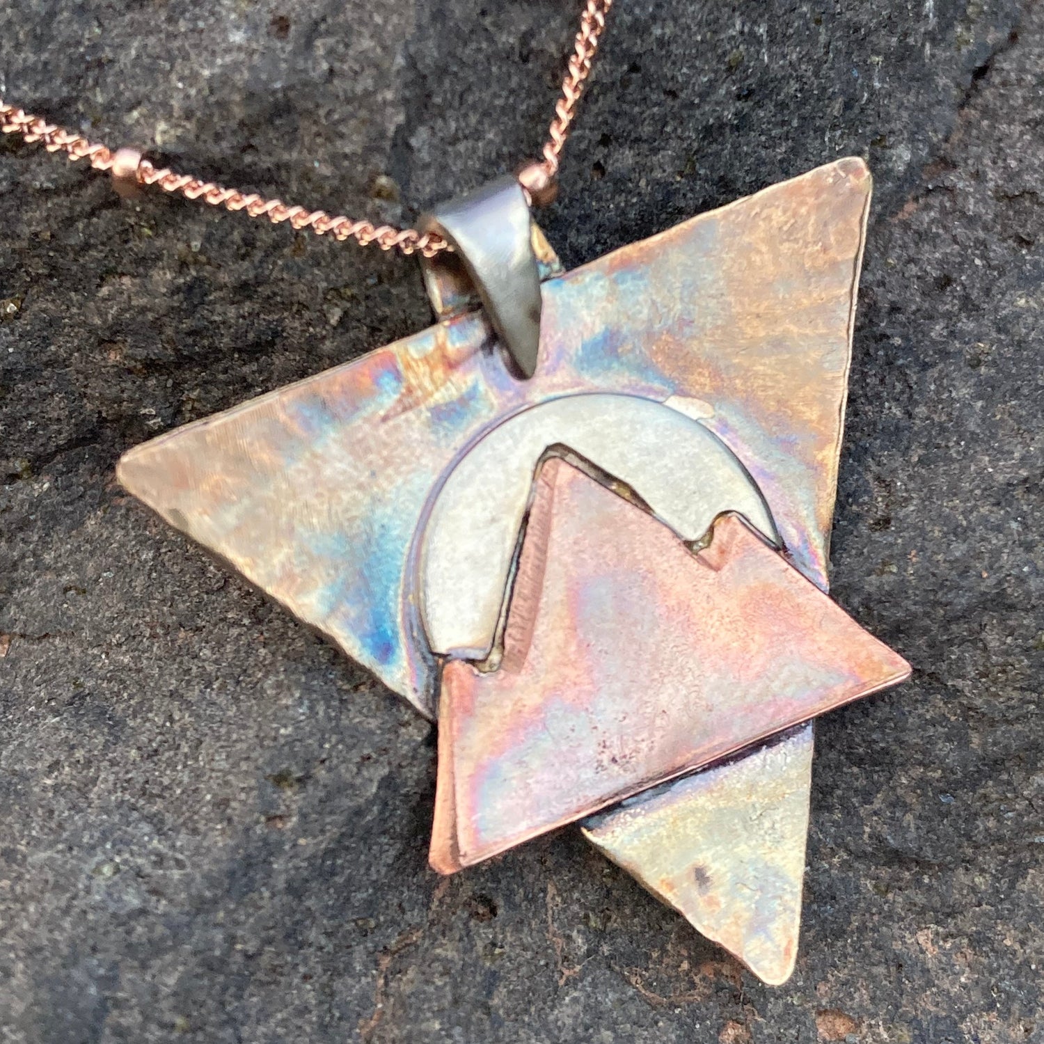 Geometric pendant necklace on a dark stone surface