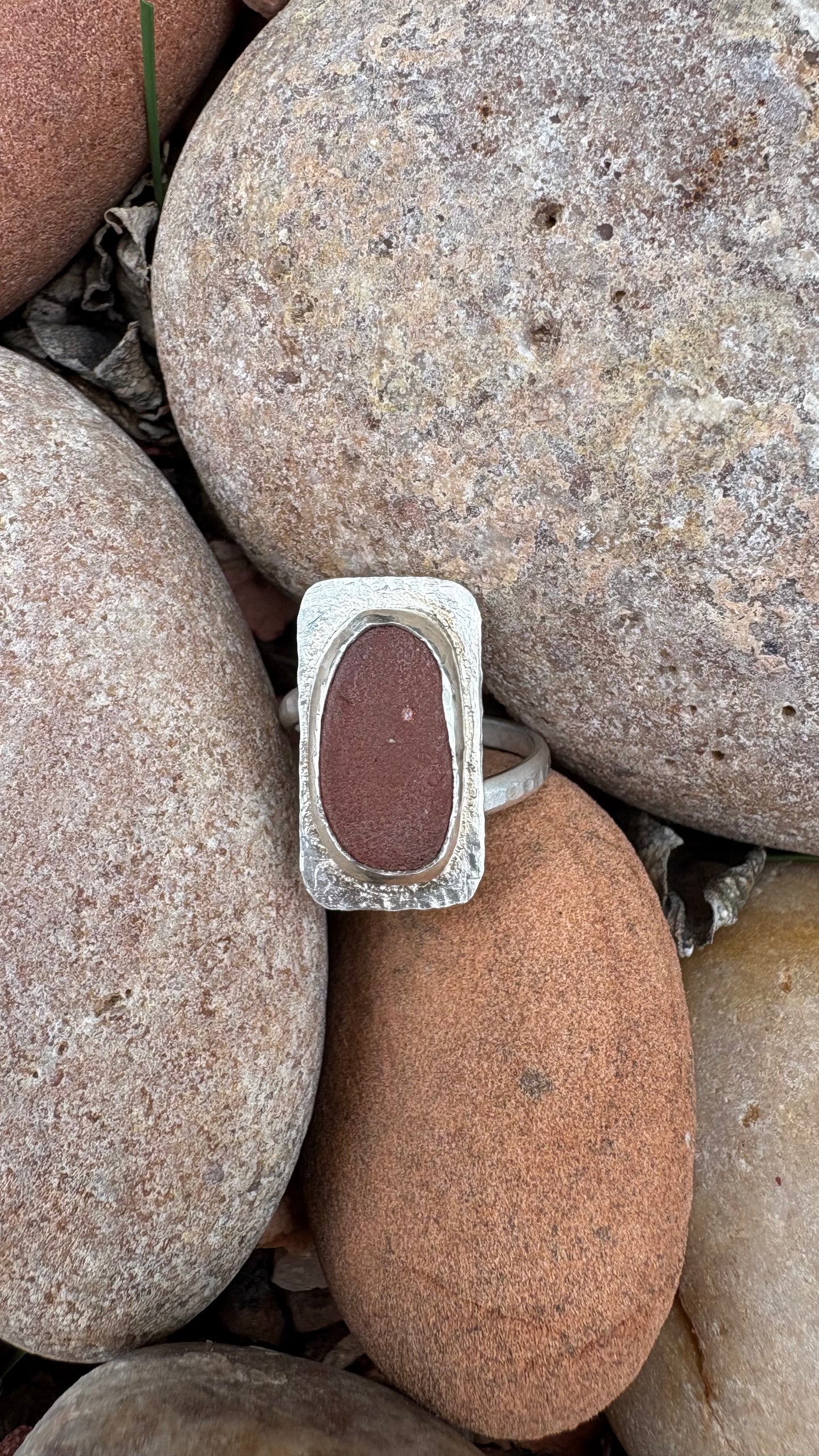 Silver ring with a red stone on a bed of rocks