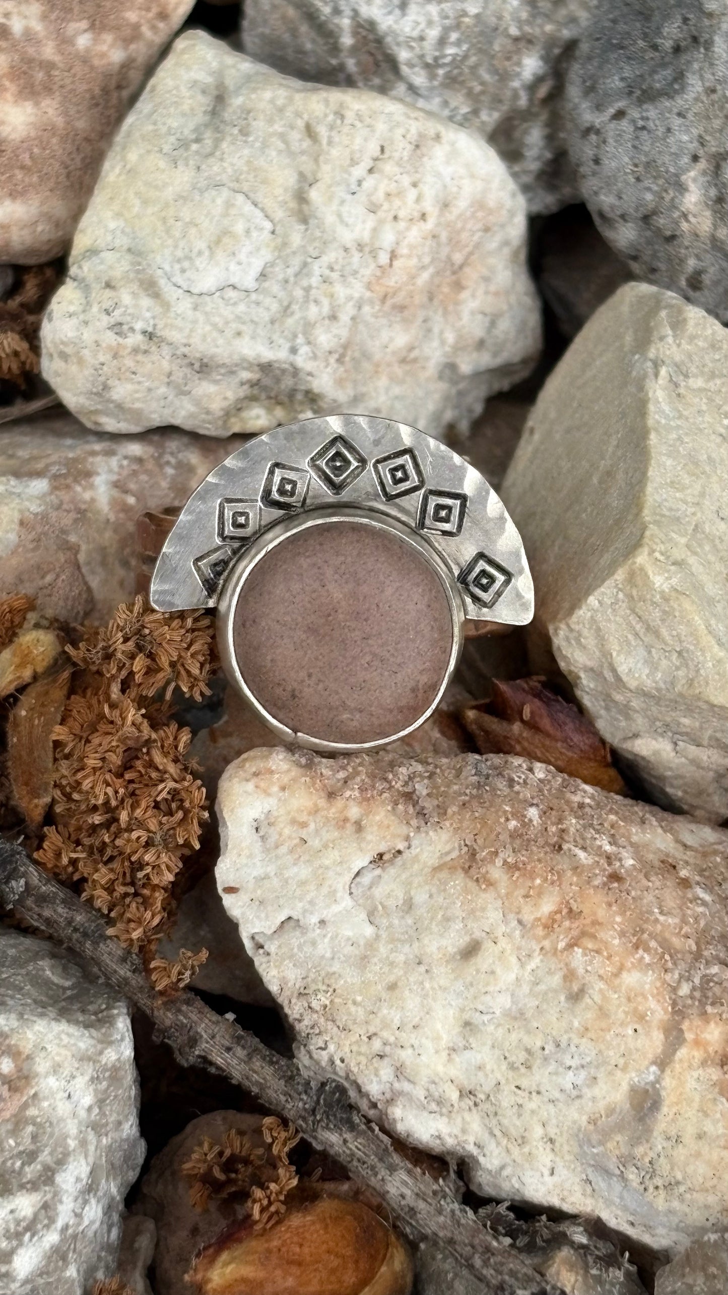 Silver ring with geometric design on a bed of stones and leaves